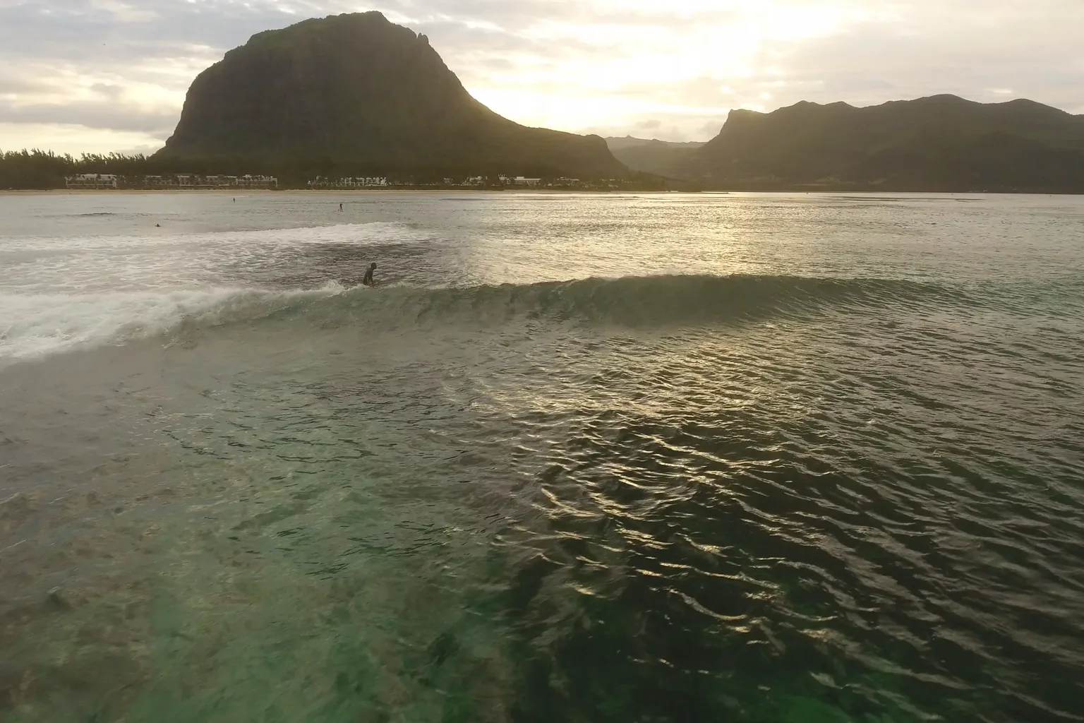 Drone view over the Le Morne lagoon at sunrise, a surfer paddling and the mountain behind.