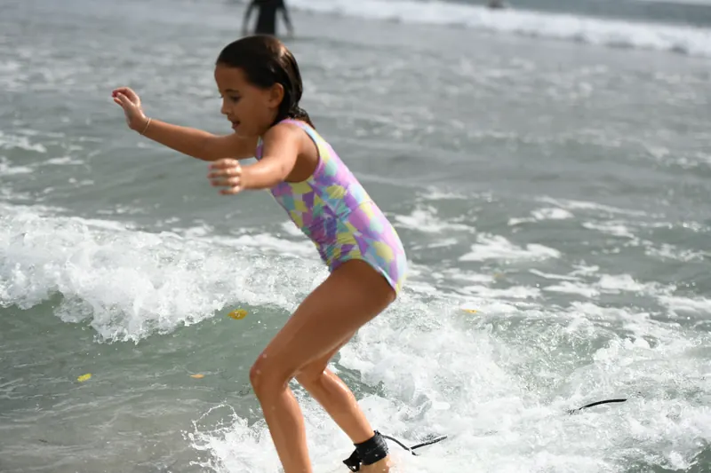 A Duckling rides the whitewater to the beach, arms out.