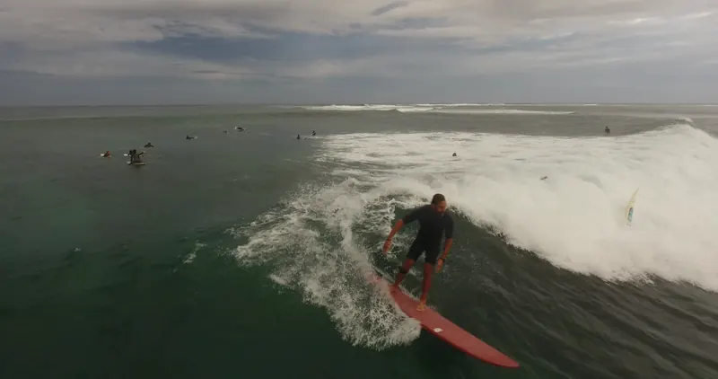 A surfer on a red board drops into a Le Morne wave, whitewater behind.