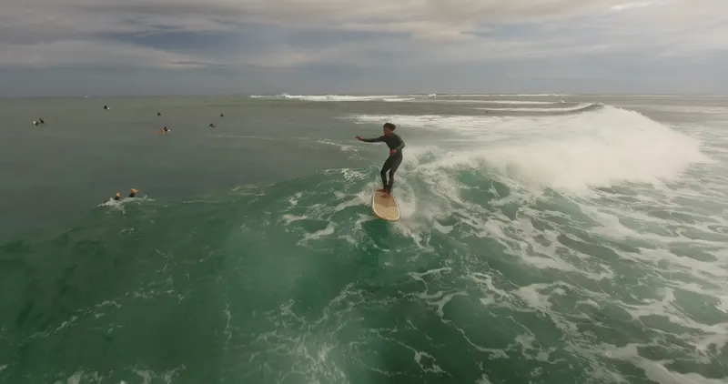 A surfer rides a glassy green wave at Le Morne, seen from the drone.